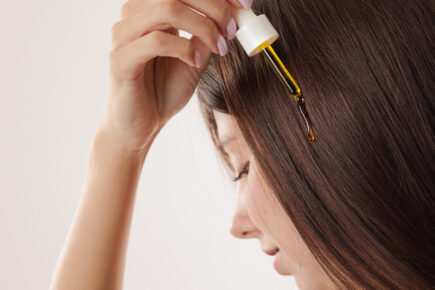 woman applying oil and serum on hair with pipette close-up, on white background, hair care concept, healthy hair